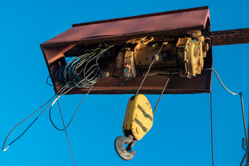 Electric cable hoist with black hook in yellow casing.