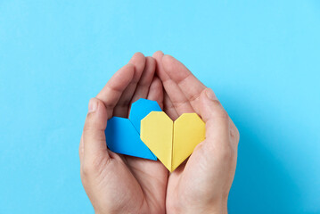 Fototapeta premium Hands holding and protecting blue and yellow origami hearts; support for Ukraine