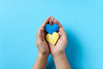 Hands holding and protecting blue and yellow paper hearts; support for Ukraine