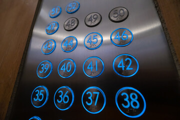 Close-up of blue glowing elevator buttons with Braille characters, numbers from the 35th floor to...