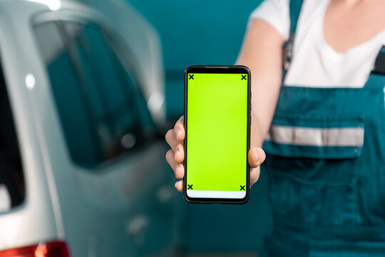 Woman mechanic in overall shows a smartphone with green chroma key. Mock up. Close up. The concept of women's equality - Powered by Adobe