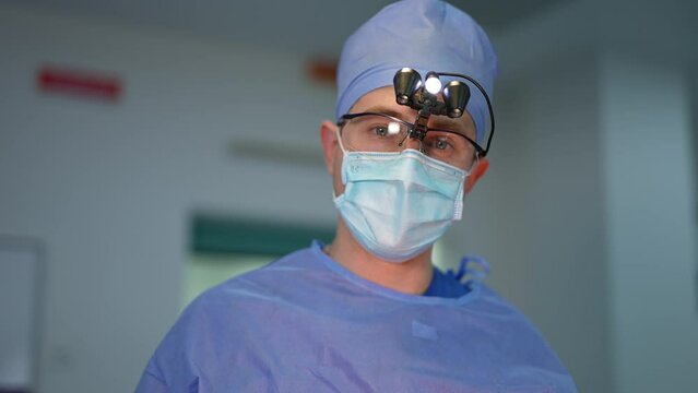 Calm confident surgeon in uniform, cap, device glasses and mask talks to the camera. Portrait of an experienced doctor close up.