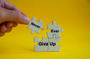 Motivational text on jigsaw puzzle with hand holding a missing jigsaw - Never ever give up. - obrazy, fototapety, plakaty