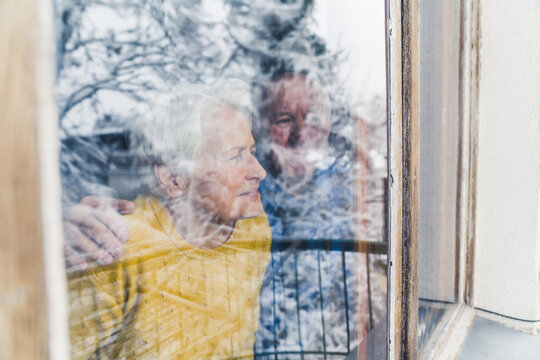 View from behind the window glass. Two caucasian retired grandparents looking outside and thinking about the future. High quality photo