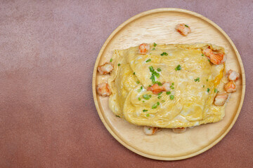 Top view of Creamy Omelet with Shrimp in wooden plate on brown table.