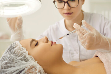 Cosmetology skin care. Cosmetologist performs rejuvenating facial injection procedure for her female client. Woman in beauty salon receiving injections to tighten and smooth wrinkles on skin.