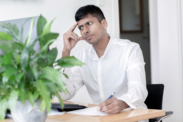 Junger Manager sitzt am Schreibtisch und überlegt
