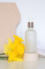 Obraz na płótnie Canvas Cosmetic bottle and flowers. Frosted bottle with pipette on the podium and a bouquet of daffodils. Cosmetic oils or alternative medicine