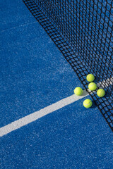 paddle tennis balls by the net on a blue paddle tennis court