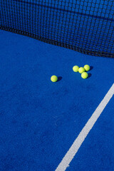 several paddle tennis balls by the net on a blue paddle tennis court