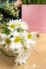 Close-up of beautiful white daisies on the table, in the background a florist makes a flower arrangement in a pink box. Vertical photo