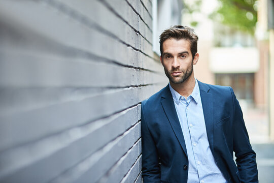 Hes got the look. Shot of a handsome young businessman standing against a grey facebrick wall.