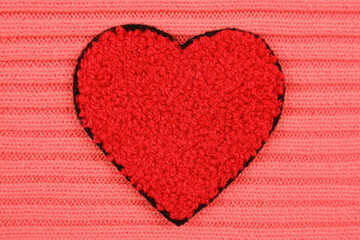 A red heart made of wool lies on a pink knitted background.Handmade concept, needlework, favorite hobby, sale of yarn for knitting.Cozy background for Valentine's Day greeting cards