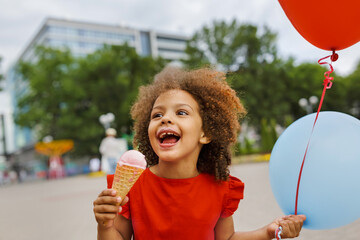 a black laughing child with ice cream in a waffle cone at summer day