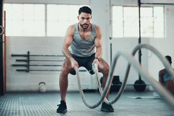 Never give up never surrender. Shot of a young man using the ropes in the gym to build arm strength.
