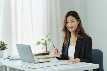 Happy woman sitting at desk, working on computer at home. Pleasant attractive smiling lady looking at camera. © PaeGAG