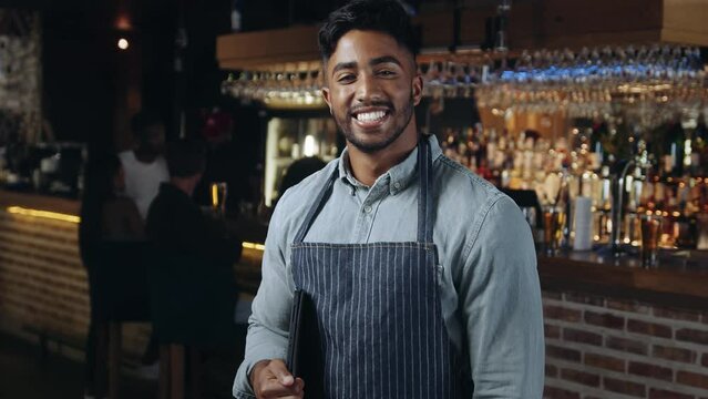 Man who works at a restaurant looking at tablet and smiling and then smiles at camera. 