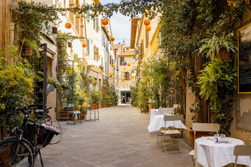 Fototapeta na wymiar Beautifully landscaped narrow street with restaurant tables in the old town of Grosseto, in Maremma region of Italy. Cozy city view of the old Italian town