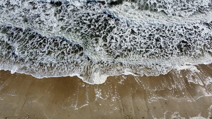 Aerial drone view flight over sea waves that roll onto sandy shore. Top view. Waves with white foam hit sandy shore. Slow motion. Nature, natural background. Concept eco, environment, climate change