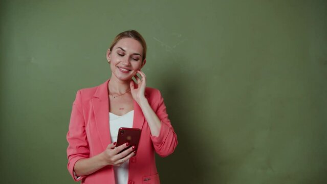 Blonde girl in a pink jacket looks at the phone and smiles.