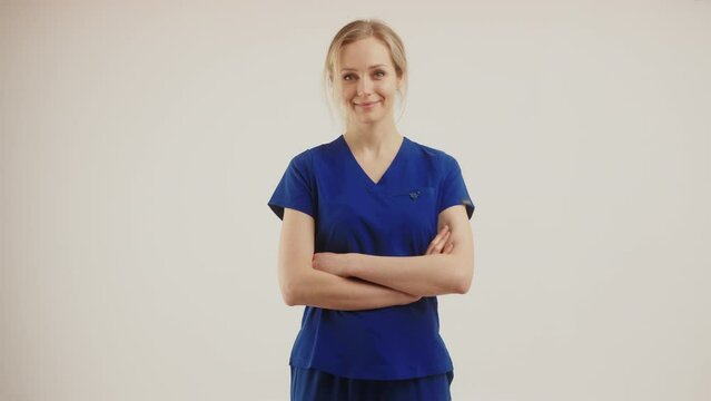 satisfied blonde Caucasian nurse with arms crossed and nodding medium shot isolated studio shot copy space medical concept. High quality 4k footage