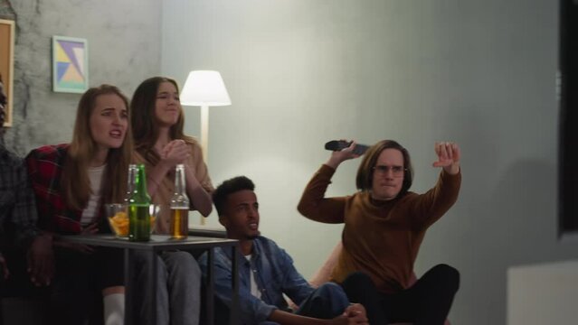 Aggressive guy breaks TV set throwing remote controller after favorite team loss visiting friends place slow motion. Angry supporters disappointed with failed game