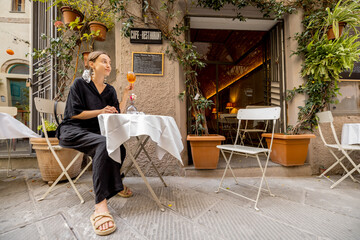 Young woman sitting with Spritz Aperol drink at italian restaurant on cozy street outdoors. Concept...