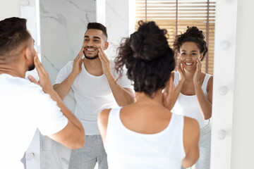 Family Beauty Care. Young Arab Spouses Using Moisturising Face Cream Near Mirror