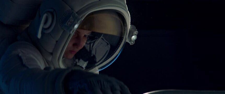 Female astronaut performing spacewalk, working on a outer part of a space craft. Shot with 2x anamorphic lens