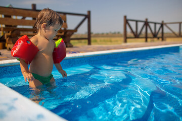 Boy with armbands playing with toys near the pool with clear water on the background of a summer...