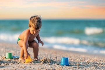 Boy playing with toys on the beach building beads and turrets smiling at someone behind the scenes on summer vacation
