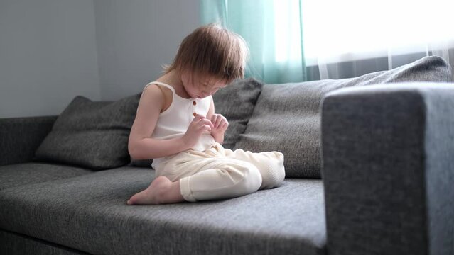 Cute girl child toddler on the couch is sad and upset. Sad child alone on the sofa in the living room, childish emotions