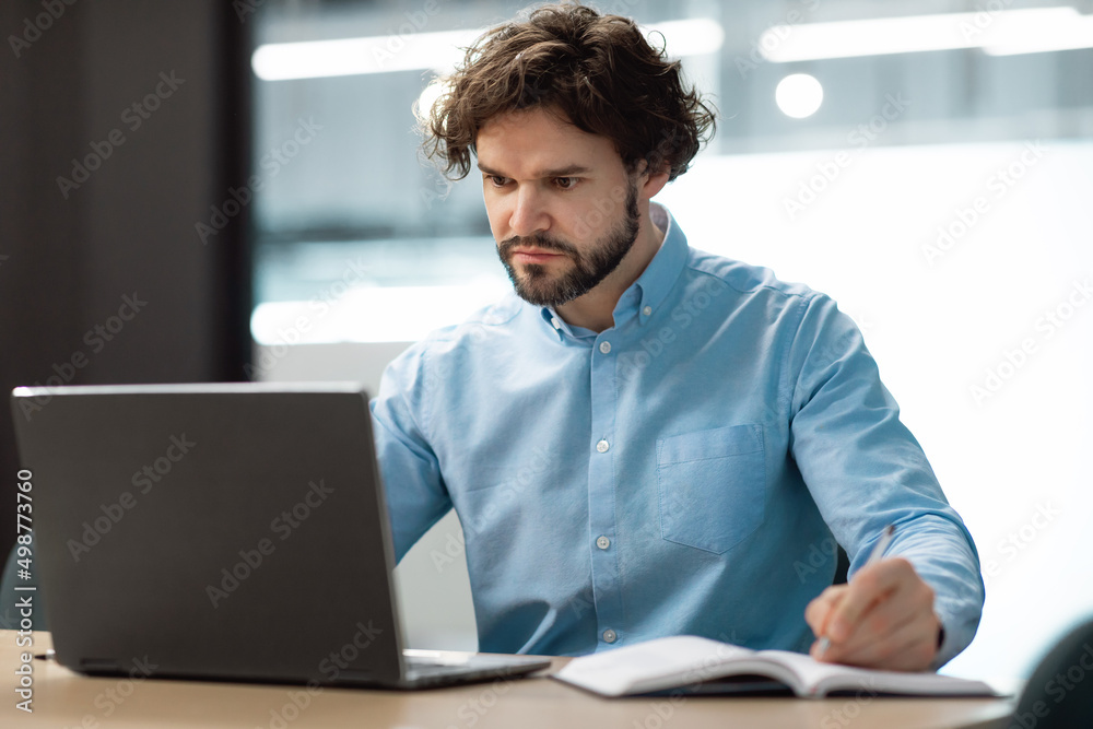 Aufkleber portrait of focused man using laptop and writing in notebook