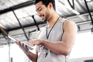 Im tracking your progress. Shot of a handsome young man using a digital tablet at the gym.
