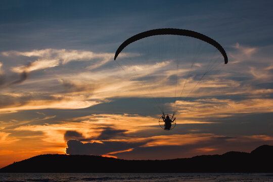 silhouette paramotor or paraglider fly over the sea with beautiful sunset sky background.