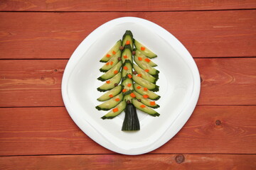 Concept of a Christmas tree on a white plate. from a cucumber. snowflakes. on a wooden background.