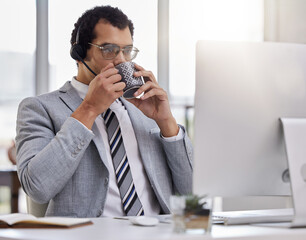 Gearing up to make some big sales. Shot of a young call centre agent drinking coffee while working on a computer in an office.