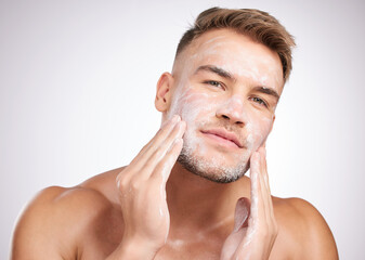 My skin loves this product. Studio shot of a young man washing his face against a grey background.