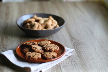 Plate of chocolate chip cookies and bowl of sugar cookies on wooden table. Selective focus.