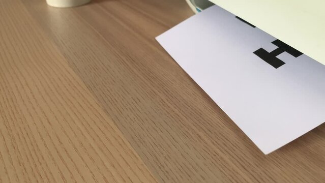 Printing &ldquo;NOW HIRING&rdquo; text written message on paper sheet document. Close up A4 page being printed from multifunction printer scanner on wooden desk in office. Male hand take paper from printer