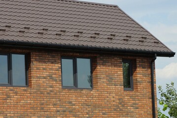 part of a brown brick wall with windows under a tiled roof against a blue sky