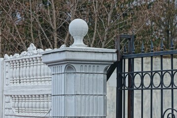 part of a white concrete column with a stone ball in a black iron fence with sharp bars on the street