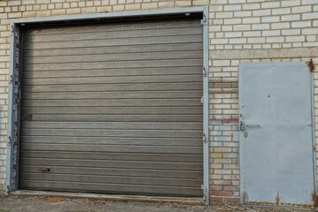 brown gate and gray metal door on a white brick wall of a garage outside