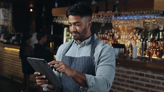 Man who works at a restaurant looking at tablet and smiling.