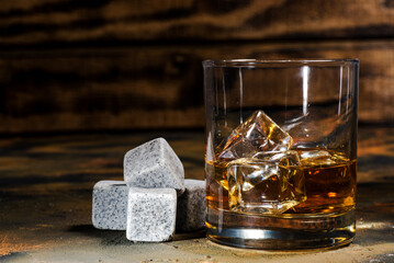 cold stones for whiskey and a glass of whiskey close-up on an old table.