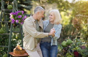 Joyful senior spouses dancing in the garden, holding hands and laughing, enjoying spending time...