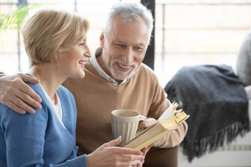 Elderly married couple laughing and reading book