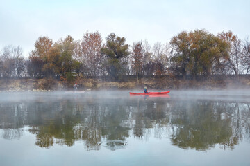 Landscape with women paddling red kayak and stand up paddle board at autumn misty river near shore with yellow trees