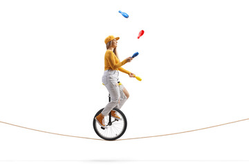Young female riding a unicycle on a tightrope and juggling