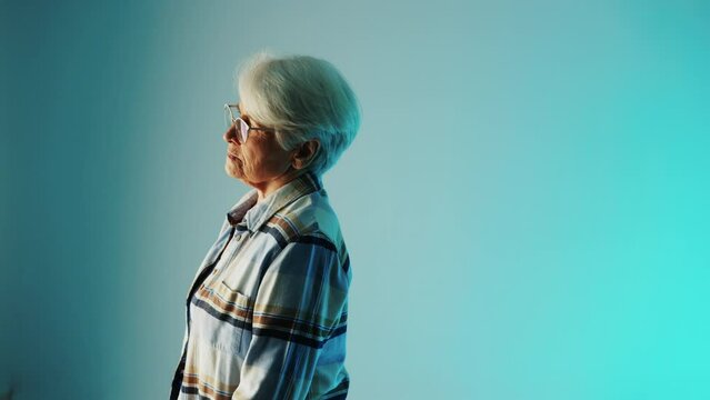 senior European woman with white hair and glasses standing sideways and thinking about a disease she has copy space blue background medium closeup healthcare concept. High quality 4k footage